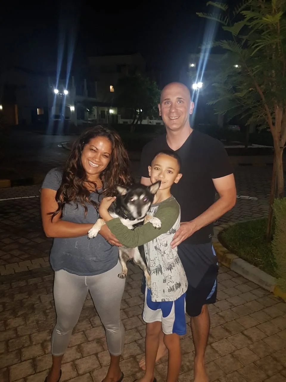 A family smiling together while their child holds a small dog