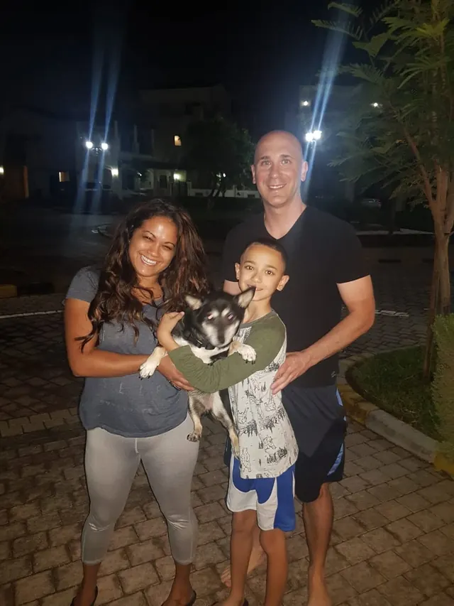A family smiling together while their child holds a small dog