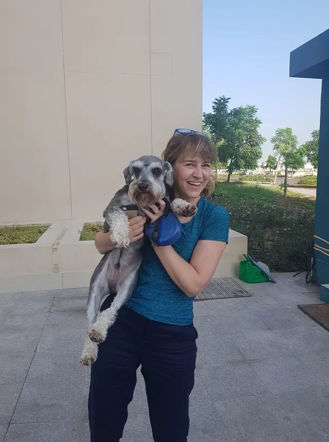 A smiling woman holding her grey dog outdoors