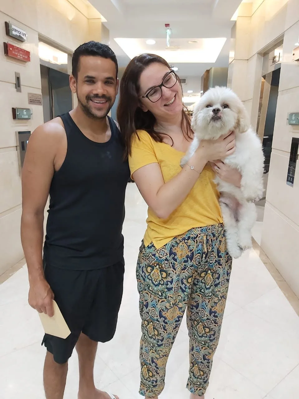 A smiling couple holding their white dog.